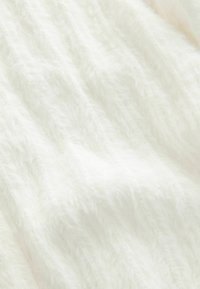 Vit, fluffig textil med en mjuk struktur och subtil lyster. Den har ett vågigt mönster som skapar djup och visuell intress.