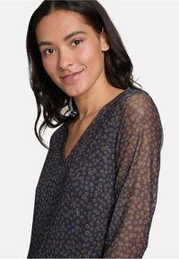 Durchsichtige marineblaue Bluse mit Punkten, tiefem V-Ausschnitt und langen Ärmeln. Weicher Textur, leichtes Material und leicht lockere Passform.