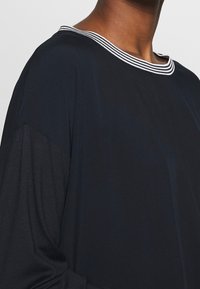 Långärmad topp i mörk marinblått tyg, med en bred krage i vita ränder, som visar en mjuk textur och avslappnad passform.