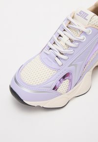 Zapatillas de deporte de color púrpura claro con tela de malla, diseño elegante y acentos texturizados. Presentan cordones blancos y un detalle plateado en la suela.