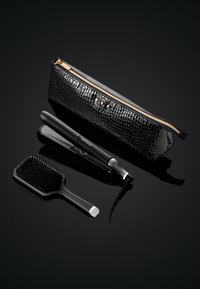 Zwarte tas met krokodillenpatroon en gouden rits, met daarin een stijltang en een zwarte haarborstel met plastic haren en een gladde handgreep.