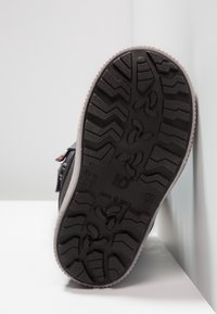 Semelle de chaussure noire présentant un motif de semelle texturé avec des zones pour la traction, bord contrastant gris clair. Fabriqué en Italie.