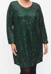 Grön paljettklänning med långa ärmar, rund halsringning och en lös passform. Har ett texturerat mönster med varierande storlekar på paljetterna genom hela klänningen.