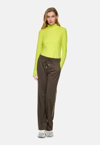Long-sleeve, high-neck top in bright neon yellow, paired with brown, elastic-waist pants featuring side stripes and a textured pattern.