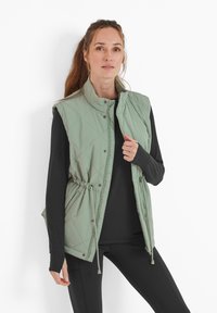 Quilted light green vest with stand-up collar, snap closure, drawstring waist, and side pockets, worn over a black long-sleeve shirt.