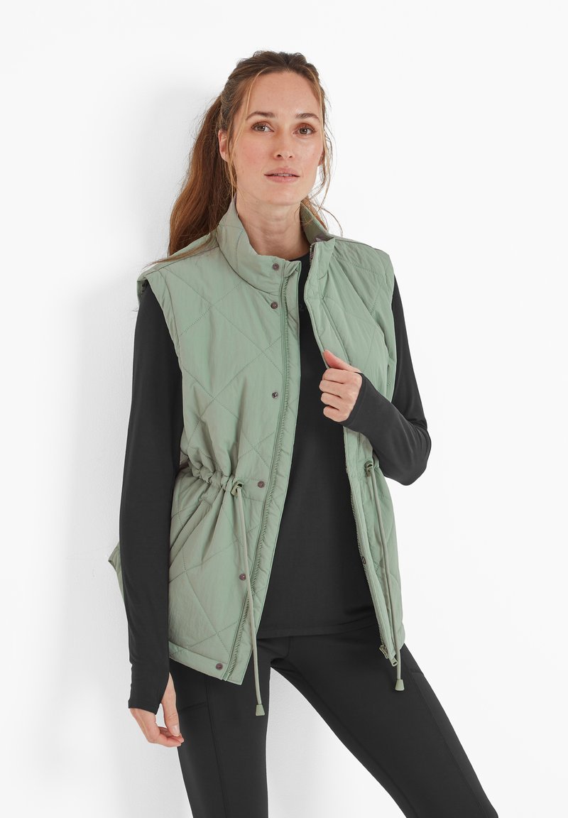 Quilted light green vest with stand-up collar, snap closure, drawstring waist, and side pockets, worn over a black long-sleeve shirt.
