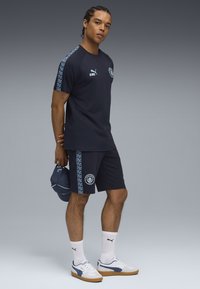 Marinebl�åt sportstøj bestående af kortærmet skjorte og shorts, begge med mønstrede sidekanter. Hvide sneakers og en marineblå kasket fuldender looket.