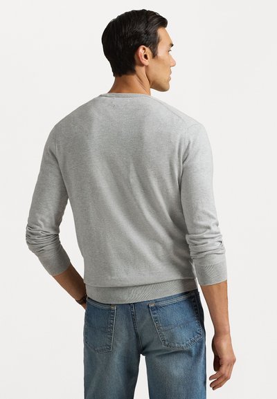 Sweater cinza feito de tecido de malha com mangas longas, decote redondo e punhos canelados. Combinado com jeans de algodão azuis. Design simples e clássico.