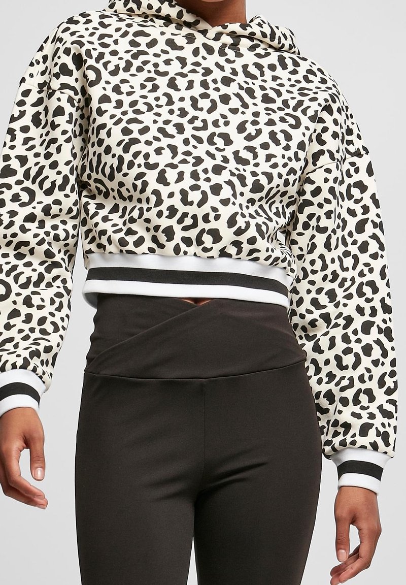 Personne portant un sweat à capuche court avec imprimé léopard noir et blanc et des leggings noirs taille haute avec un détail croisé à la taille.