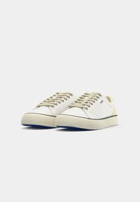 Une paire de baskets blanches basses avec des lacets beige, des semelles en caoutchouc et un petit logo "HUGO" sur le côté, présentée sur fond blanc.