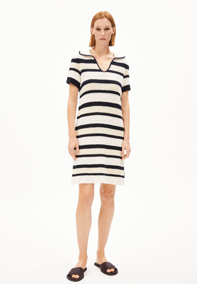 Stickad klänning med marinblå och vita horisontella ränder, korta ärmar, V-ringning och A-linjeformad siluett. Kompletterad med svarta slidesandaler.