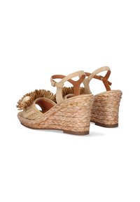 Sandalias de cuña con un tacón de yute trenzado, correa en el tobillo beige y un acento floral texturizado. Materiales naturales y una paleta de colores neutros.