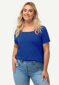 Blusa azul real de manga corta con escote cuadrado, hecha de una tela suave. Combinada con jeans azul claro que presentan sutiles detalles de cremallera.