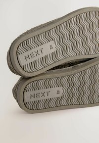 Graue Gummischuhsohlen mit einem wellenförmigen Profil. "NEXT" und die Größe "42" sind seitlich eingraviert, mit strukturierten Oberkanten.