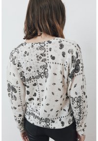 Pull léger beige clair avec un motif paisley et floral noir, tissu texturé, manches longues et encolure arrondie.