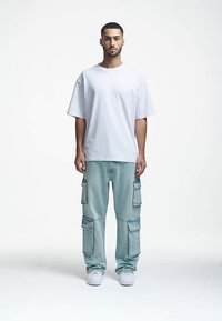 T-shirt branca de tamanho grande combinada com calças cargo azul claro com vários bolsos e ajuste descontraído. Ténis brancos completam o visual.