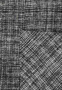Tekstura ima kontrastni houndstooth vzorec v črni in beli barvi. Tkanina ima mehak, teksturiran občutek z večplastno dimenzionalnostjo.