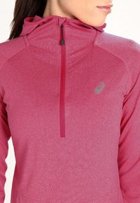 Pullover sportivo rosa con cappuccio, caratterizzato da una zip frontale a metà, materiale elastico e un logo discreto sul petto.