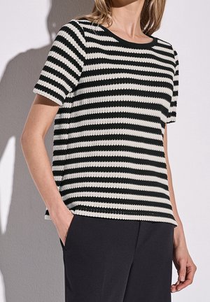 Zwart-wit gestreept gebreid shirt met korte mouwen, een ronde hals, een gestructureerde stof en lichte zijslits, gedragen met een donkere broek.