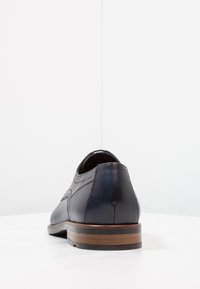 Black leather shoe with a rounded heel and a smooth finish, featuring subtle stitching details and a wooden sole with a red accent.