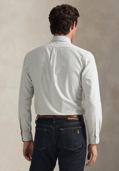 Žali dryžuoti marškiniai su apykakle, ilgomis rankovėmis ir užsegamais rankogaliais, derinami su tamsiais džinsais. Išskirtinės nugaros juostos detalės.