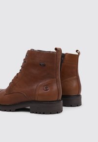 Botas de tobillo de cuero marrón con un acabado texturizado, parte delantera con cordones, cremallera lateral y suela de goma con un patrón distintivo.