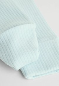 Lyseblåt ribbet stof med en blød tekstur; foldede manchetter med et ensartet ribmønster, der skaber et lagdelt udseende.