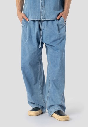 Pantalones vaqueros de pernera ancha en azul claro con cintura elástica y cordón. Con dos bolsillos laterales y un ajuste relajado, combinados con zapatos tejidos sin cordones.