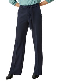 Marineblauwe wijde broek van gladde stof, met een ceintuur in de taille, plooien aan de voorkant en een getailleerde snit. Zwarte schoenen complementeren de outfit.