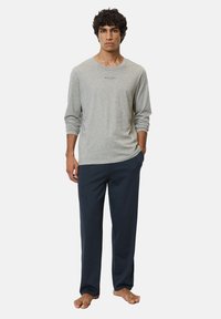 Chemise grise à manches longues avec un col rond et un logo sur la poitrine, associée à un pantalon large bleu foncé. Les deux sont fabriqués dans un tissu doux.