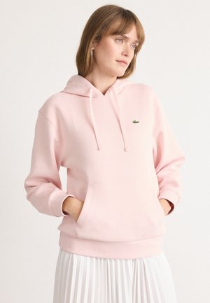 Lys rosa hettegenser med en frontlomme, ribbede mansjetter og en liten grønn brodert logo på venstre bryst.