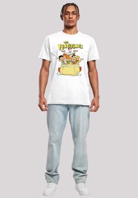 Hvit bomull t-skjorte med en fargerik tegneserieprint av karakterer i en bil, med "The Flintstones" tekst over. Modellen har på seg lyse denim jeans.