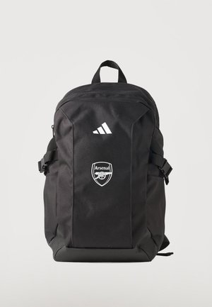 Sac à dos noir Adidas avec l’écusson du club de football Arsenal, sangles de compression latérales et poignée de transport supérieure sur fond uni.
