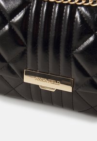 Black quilted handbag with a shiny texture, featuring a gold-tone logo plate and chain strap, highlighting its geometric pattern and sophistication.