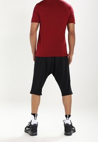 Camiseta roja de manga corta combinada con pantalones cortos negros de corte holgado que caen por debajo de la rodilla. Zapatillas deportivas negras con detalles en blanco.
