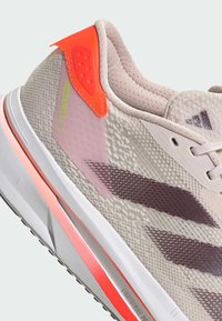 Světlobéžová sportovní bota s oranžovým zadním pruhem, fialovými detaily a texturovanou látkou, na boku označená nápisem "ADIZERO SL 2".