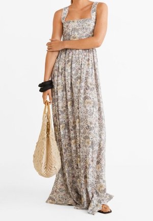 Kobieta w długa sukienka bez rękawów w kwiatowy wzór, trzyma beżową tkana torbę typu tote i czarne gumki do włosów na nadgarstku.