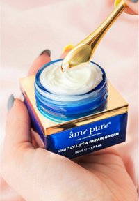 Nattlyftande och reparerande kräm i en blå glasburk med guldkant. Vit kräm skopas upp med ett guldverktyg. 50 ml storlek angiven.