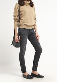 Suéter de cuello alto beige, pantalones ajustados de corte slim en color carbón, mocasines negros y un bolso bandolera negro. Tejido suave, diseño sencillo, hardware mínimo.