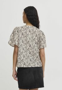Bluse mit Blumenmuster in Creme- und dunklen Tönen, mit lockerer Passform und rundem Ausschnitt. Dazu ein schwarzer Jeansrock.