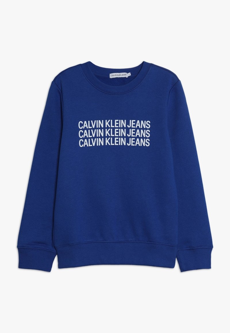 Blue sweatshirt with crew neck and ribbed cuffs. Features repeated "CALVIN KLEIN JEANS" text in white across the chest. Soft fabric texture.