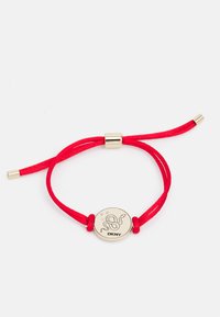 Rød stoffarmbånd med et gullfarget sirkulært charm preget med et slangedesign og "DKNY" logo, sikret med gullaksenter.