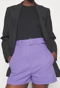 Black blazer over a fitted black top. Purple shorts with a triangular silver buckle on the belt, featuring side pockets and a smooth texture.