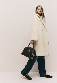 Cream oversized coat, black handbag with charm, dark jeans, and black flats. Soft texture, structured design, and contrasting colors.