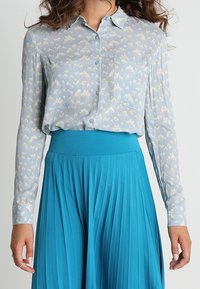 Camicia azzurra chiara con un piccolo motivo floreale, abbinata a una gonna plissettata turchese a tinta unita con una vita ampia.