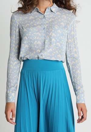 Camisa de botón azul claro con un pequeño patrón floral, combinada con una falda plisada turquesa sólida que tiene una cinturilla ancha.