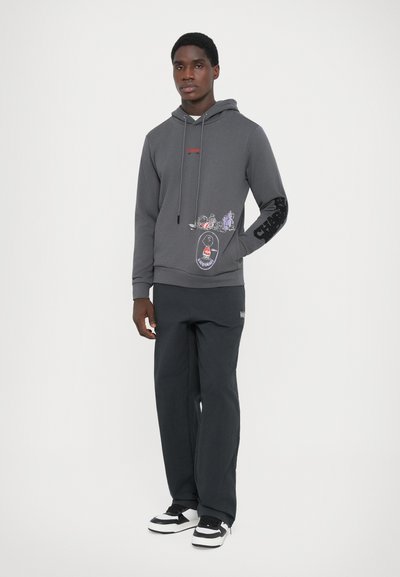 Gray hooded sweatshirt with graphic designs, black accents on the sleeves, and paired with dark pants and black-and-white sneakers.