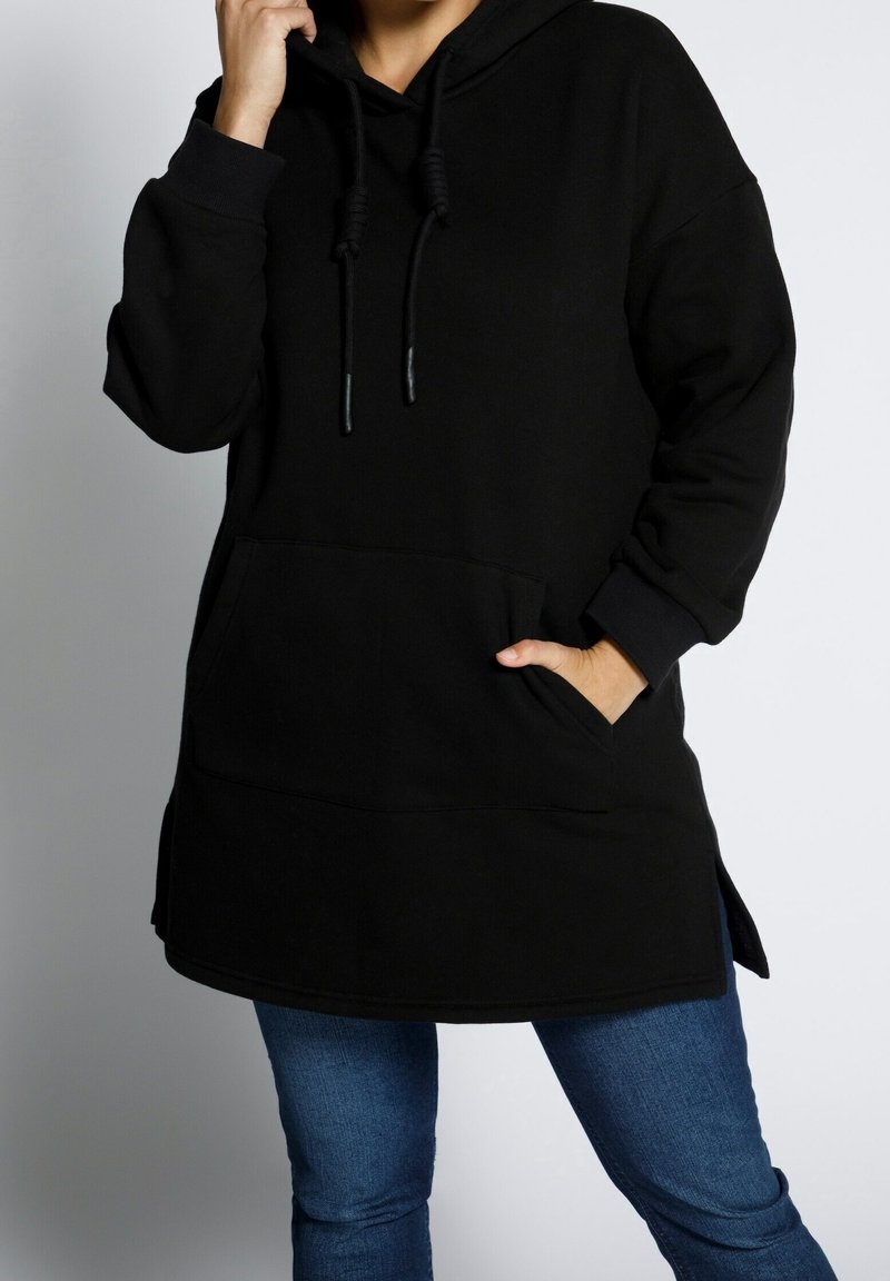 Sudadera negra larga hecha de material suave, con un bolsillo frontal, cordones ajustables y aberturas laterales para facilitar el movimiento.