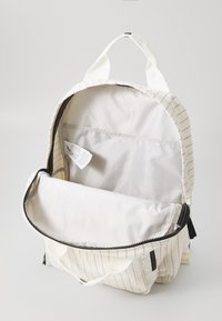 Rucsac din pânză cu exterior alb și model cu dungi roșii. Închidere cu fermoar, deschidere largă și compartiment interior cu căptușeală netedă.