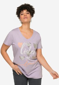 Camiseta de color lavanda con escote en V, con gráficos de corazones en plata y rosa, y el texto "escucha al amor", hecha de suave tela de algodón. Manga corta.